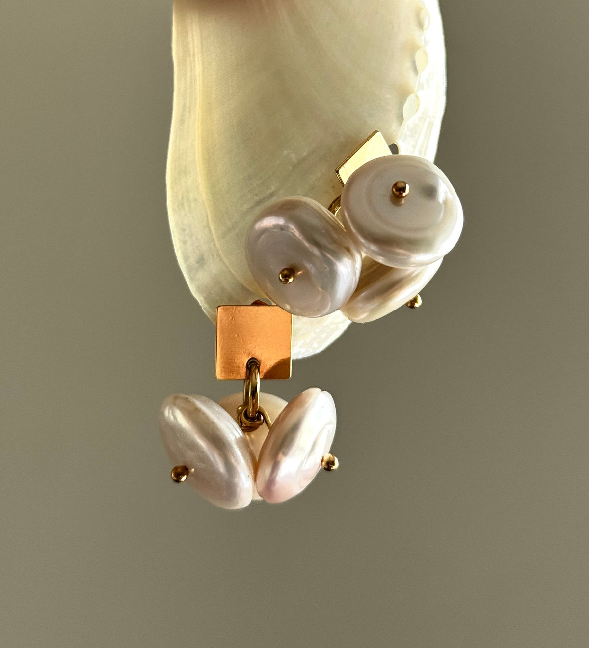 Coin Pearl Earrings by Claudine Artisanal, square gold studs with a cluster of three coin pearls, displayed on an abalone shell