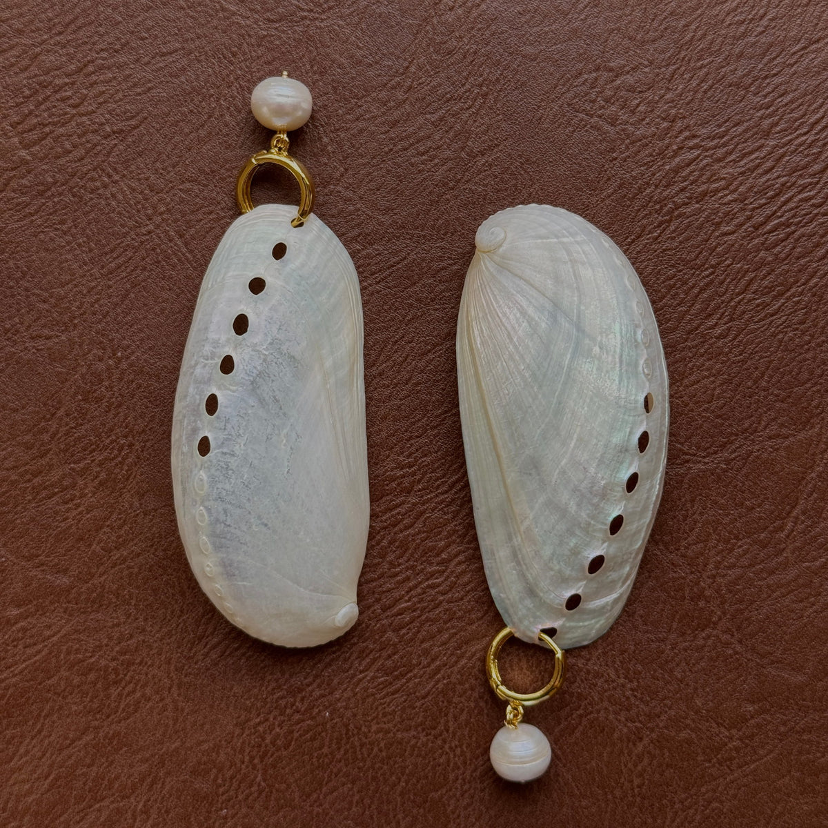 Potato Pearl Hoops by Claudine Artisanal, gold huggie hoops with small freshwater pearl drops, displayed on two abalone shells